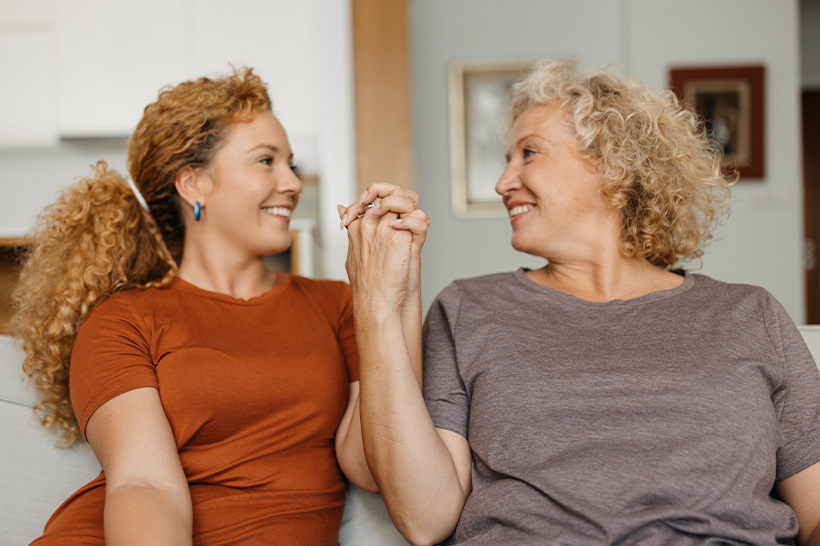 Two women sitting side by side, holding hands and smiling at each other